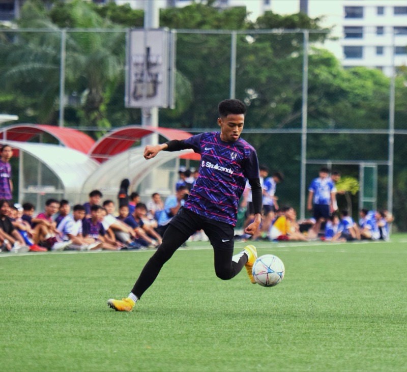 A player striking the ball as spectators watch from the touchline