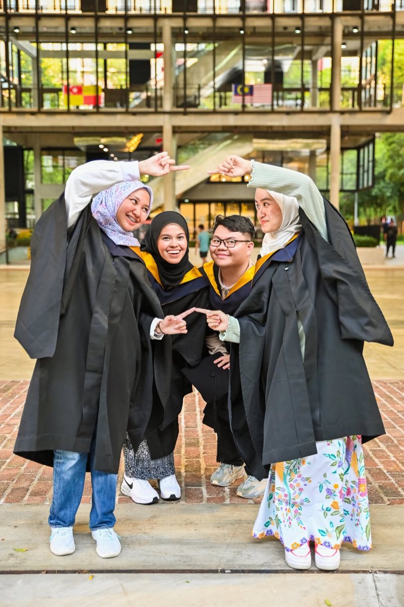 Four graduates in gowns posing together on campus