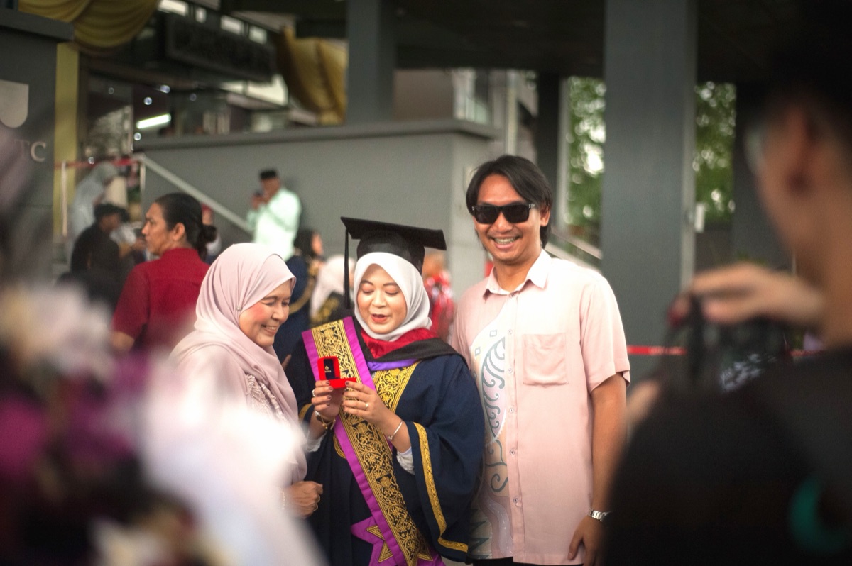A graduate holding her mortarboard, glancing over her shoulder