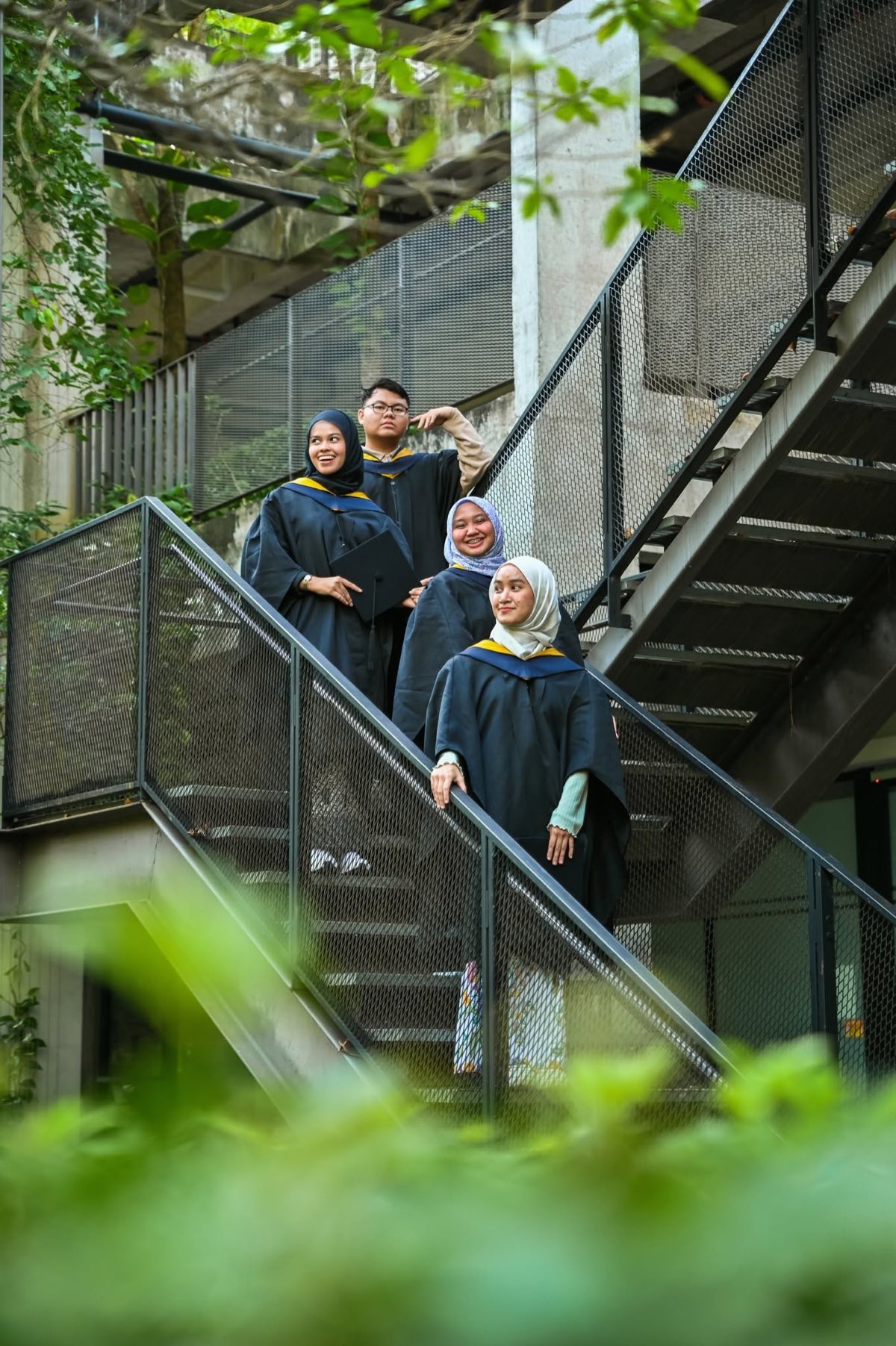 Graduates on a campus staircase framed by foliage